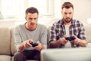 auf Spiel konzentriert. Zwei konzentrierte junge Männer spielen Videospiele, während sie auf dem Sofa sitzen foto