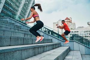 Gut aussehendes junges Paar in Sportkleidung, das springt und joggt, während es auf den Stufen im Freien trainiert foto