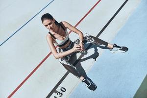 auf dem Weg zum Erfolg. Draufsicht einer jungen Frau in Sportkleidung, die sich ausruht, während sie draußen auf der Laufbahn sitzt foto