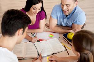 studieren macht spass. Draufsicht von vier selbstbewussten Studenten, die lernen, während sie zusammen am Schreibtisch sitzen foto