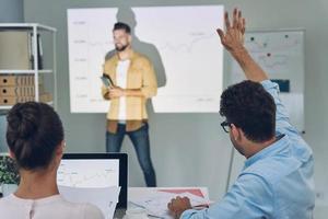 Gruppe junger moderner Menschen in eleganter Freizeitkleidung, die Daten auf der Projektionsleinwand im Büro analysieren foto