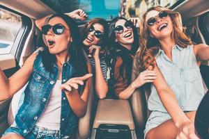 zusammen Spaß haben. Vier schöne junge, fröhliche Frauen, die glücklich und verspielt aussehen, während sie im Auto sitzen foto