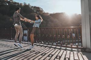 verspieltes Paar. in voller Länge vom schönen jungen Paar, das Händchen hält und sich dreht, während es draußen auf der Brücke steht foto