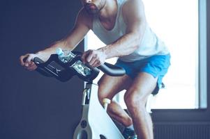 Radfahren und Energie. teil des jungen mannes in sportbekleidung, der im fitnessstudio radfährt foto