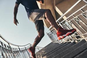 in Bewegung. Nahaufnahme eines jungen afrikanischen Mannes in Sportkleidung, der beim Training im Freien die Treppe hinunterläuft foto