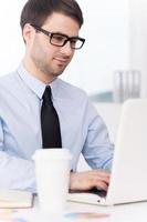 Geschäftsmann am Arbeitsplatz. hübscher junger mann in hemd und krawatte, der am laptop arbeitet, während er an seinem arbeitsplatz sitzt foto