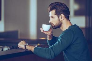 nichts ist besser als eine Tasse frischen Espresso. Seitenansicht eines hübschen jungen Mannes, der Kaffee trinkt, während er am Tresen sitzt foto