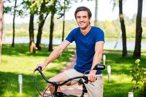 Reiten mit Vergnügen. hübscher junger Mann, der im Park Fahrrad fährt und lächelt foto