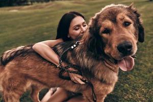 Schöne junge Frau, die die Augen geschlossen hält, während sie mit ihrem Hund im Freien spielt foto