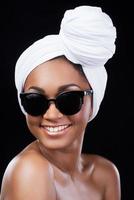 positiver und ungewöhnlicher Stil. Schöne afrikanische Frau, die ein Kopftuch trägt und lächelt, während sie in die Kamera schaut und vor schwarzem Hintergrund steht foto
