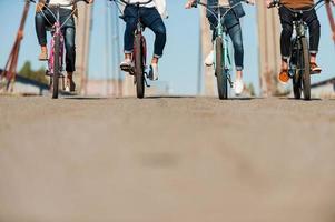 freundliche Fahrt. Zugeschnittenes Bild von vier Personen, die Fahrräder entlang der Brücke fahren foto