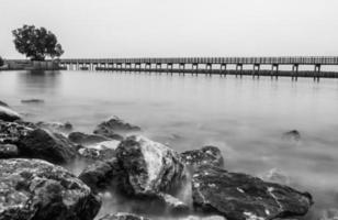 Schwarzweiss-Foto der Holzbrücke entlang des Strandes foto