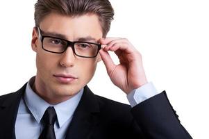selbstbewusster Blick. Porträt eines selbstbewussten jungen Mannes in Abendkleidung, der seine Brille anpasst und in die Kamera schaut, während er isoliert auf Weiß steht foto