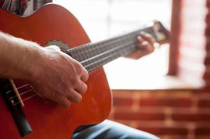 Akustikgitarre spielen. Nahaufnahme eines Mannes, der Akustikgitarre spielt, während er vor dem Fenster sitzt foto