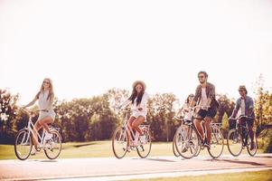Radfahren mit Spaß. Gruppe junger Leute, die Fahrräder entlang einer Straße fahren und glücklich aussehen foto