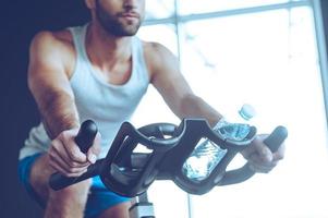 Radfahren im Fitnessstudio. Teil der niedrigen Winkelsicht eines jungen Mannes in Sportbekleidung, der im Fitnessstudio radfährt foto