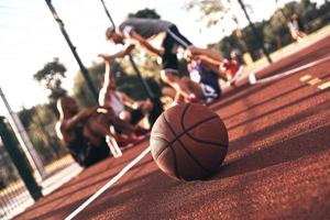 das Spiel ist vorbei. Gruppe junger Männer in Sportkleidung, die kommunizieren, während sie draußen auf dem Basketballfeld sitzen foto