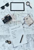 Urlaub planen. Hochwinkelaufnahme von Sonnenbrille, Fotokamera, Kompass, Lupe, Papier mit schriftlicher Checkliste und Reisepass auf der Karte foto