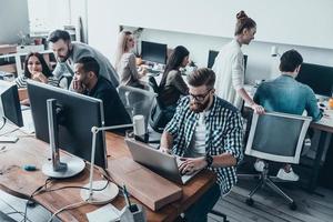 konzentriert bei der Arbeit. Gruppe junger, schöner Menschen, die Computer benutzen und kommunizieren, während sie gemeinsam im Büro arbeiten foto