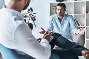 was soll ich tun, junger frustrierter mann, der spricht und gestikuliert, während er in der therapiesitzung mit dem psychologen sitzt foto