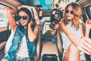 fahren mit freunden macht immer spaß vier schöne junge fröhliche frauen, die glücklich und verspielt aussehen, während sie im auto sitzen foto