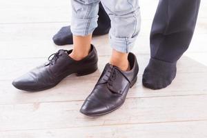 etwas überdimensioniert. Nahaufnahme eines Kindes, das große Schuhe trägt, während sein Vater in Socken neben ihm steht foto