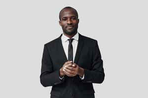 hübscher junger afrikanischer mann in formalwear, der kamera anschaut und lächelt, während er vor grauem hintergrund steht foto