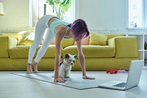 selbstbewusste junge frau in sportkleidung, die zu hause dehnübungen mit ihrem hund macht foto