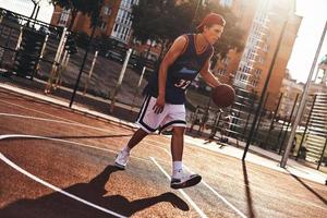 sorgloses Spiel. Volle Länge des jungen Mannes in Sportkleidung, der Basketball spielt, während er Zeit im Freien verbringt foto