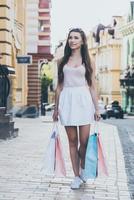 Spaß am Shoppingtag. volle Länge der schönen jungen lächelnden Frau, die Einkaufstaschen trägt, während sie die Straße entlang geht foto