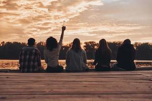 gruppe junger leute in freizeitkleidung, die selfie machen und lächeln, während sie eine strandparty am lagerfeuer genießen foto