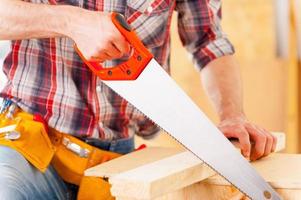 Mann sägt. Nahaufnahme des Handwerkers mit Säge in der Werkstatt foto