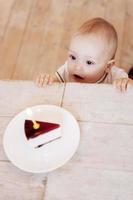 alles gute zum geburtstag draufsicht auf das süße kleine baby, das auf den teller mit kuchen schaut und den mund offen hält foto