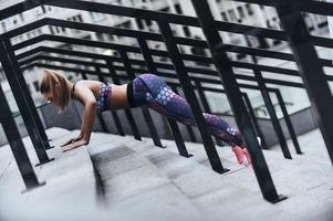 sport ist ihr lebensstil. Moderne junge Frau in Sportkleidung, die Plankenposition hält, während sie auf den Stufen im Freien trainiert foto