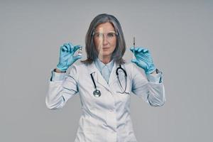 Reife schöne Ärztin im Gesichtsschutz mit Spritze foto