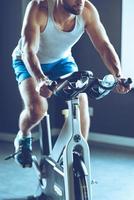 Beste Indoor-Maschine zum Abnehmen. teil des jungen mannes in sportbekleidung, der im fitnessstudio radfährt foto