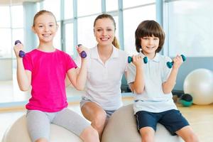 Lehrer mit Kindern. Fröhlicher Lehrer, der Kindern beim Trainieren im Fitnessstudio hilft foto