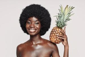 Porträt einer schönen jungen Afrikanerin, die Ananas auf der Schulter hält und lächelt foto