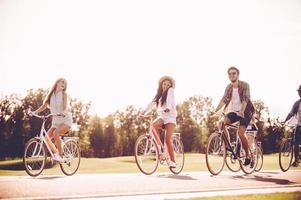 Gemeinsam Radfahren macht Spaß. Gruppe junger Leute, die Fahrräder entlang einer Straße fahren und glücklich aussehen foto