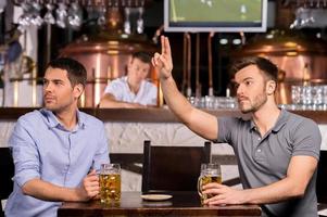 Kellner Zwei junge Männer sitzen in der Bar, während einer von ihnen einen Kellner anruft foto