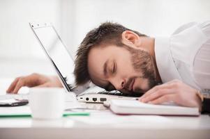 Schlafen am Arbeitsplatz. junger mann in formalwear, der am arbeitsplatz schläft foto
