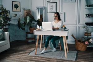 Dinge erledigen. schöne junge Frau, die mit dem Computer arbeitet, während sie im Heimbüro sitzt foto
