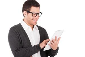 Arbeiten an einem digitalen Tablet. Fröhlicher junger Mann, der an einem digitalen Tablet arbeitet und lächelt, während er isoliert auf Weiß steht foto