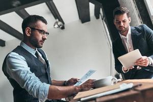 sich um das Geschäft kümmern. Zwei junge moderne Männer in Abendkleidung arbeiten zusammen, während sie drinnen sitzen foto