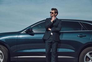 Selbstvertrauen und Charisma. hübscher junger Geschäftsmann, der die Hand am Kinn hält, während er draußen in der Nähe seines Autos steht foto