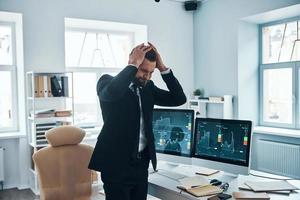 frustrierter junger mann in formeller kleidung, der während der arbeit im büro emotionalen stress durchmacht foto