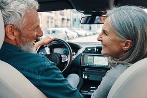 Rückansicht eines aktiven Seniorenpaares, das eine Autofahrt genießt, während es auf den Vordersitzen des Autos sitzt foto