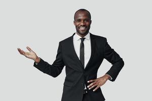 charmanter junger afrikanischer mann in formalwear, der kopienraum zeigt und lächelt, während er vor grauem hintergrund steht foto