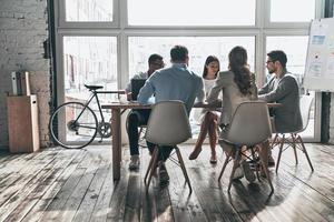 Strategie besprechen. Gruppe junger moderner Menschen in eleganter Freizeitkleidung, die während der Arbeit im Kreativbüro über Geschäfte diskutieren foto