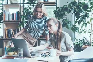 gemeinsam über ein neues Projekt sprechen. Zwei junge Geschäftsfrauen in eleganter Freizeitkleidung diskutieren etwas, während sie gemeinsam auf den Laptop schauen foto